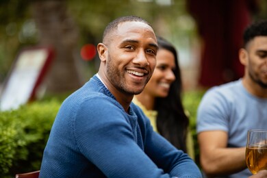 a group of friends having drinks outdoors at a bar. the main focus is a man smiling and looking at the camera.