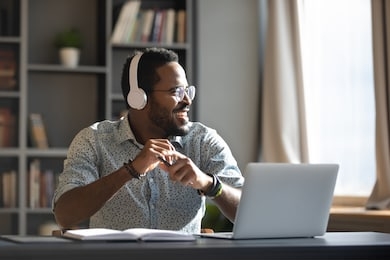 happy relaxed millennial afro american business man wear wireless headphones look away rest at workplace finished work listening music podcast feel peace of mind concept sit at desk in sunny office