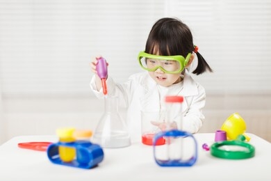 toddler girl pretend play  scientist  role  at home against white background