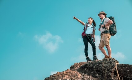 young asian couple hikers climbing up on the peak of mountain. two people hikers on top of the mountain enjoying valley view. tourists with backpacks. climbing ,helps and team work concept