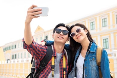 portrait of young happy asian tourist couple in casual attire taking a selfie while traveling in bangkok thailand