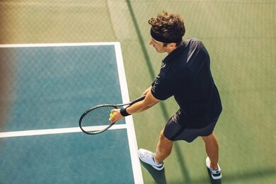 top view of a young tennis player with racket ready to serve a tennis ball. professional player standing at the baseline holding the tennis racket and the ball before starting the match on a hard cour