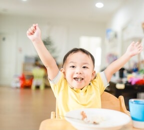 happy face and enjoy eating concept.little asian toddler boy raised hands enjoy eating with sticky rice with fork on a plate in breakfast time at home.concept for food, child development, oral health.