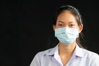 young asian woman wearing facial hygienic mask for safety on black background against infectious diseases, flu, anti-pollution, anti-smog and viruses. space for text   