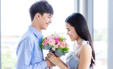valentine's day concept,asian young happy sweet couple holding bouquet of red and pink roses after lunch in a restaurant background