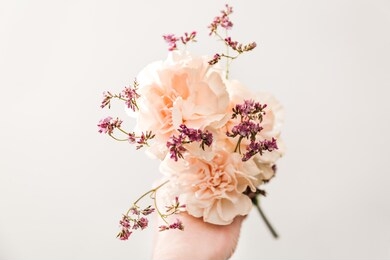 vintage bouquet of flowers in the hand on the tint blue background, symbol of love, pink or beije carnations and small decoration branch