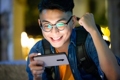 asian young man win mobile games on smart phone with fist gesture outdoor in the evening