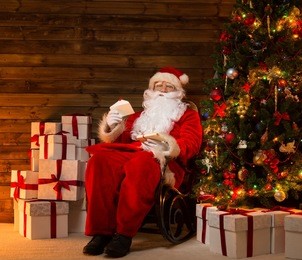 santa claus sitting on rocking chair in wooden home interior with letters in hands
