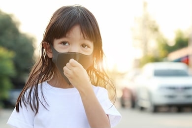 a long haired thai girl is wearing a white shirt, standing outside, wearing a black mask, protecting his face from polluted airborne dust and wearing a mask to protect against germs and viruses.
