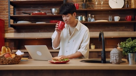 cute young man sit and use laptop work in the morning at home in kitchen portrait male morning asia asian casual chinese guy, social media internet notebook pc close up slow motion