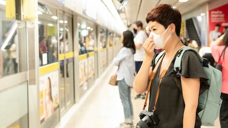 beautiful middle aged asian female traveller cover mouth and cough, wear medical face mask to protect from infection of viruses, pandemic, outbreak and epidemic of disease in crowded underground train