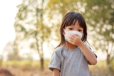 a long haired thai girl is wearing a gray shirt, standing outside, wearing a white mask, protecting his face from polluted airborne dust and wearing a mask to protect against germs and viruses.