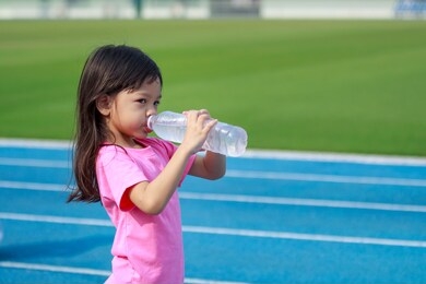 beautiful thai girl, cute, long hair, wearing a bitter dress shirt drinking water from a bottle with thirst holding two bottles of water to drink after tired from running and playing in the stadium