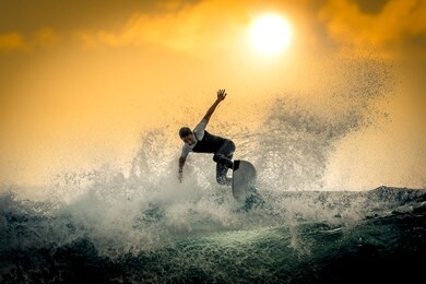 young surfer with with wetsuit enjoying big waves in tenerife, canary islands. sporty boy riding his surf board on the ocean wave. brave teenager making tricks on the rough sea during a competition.
