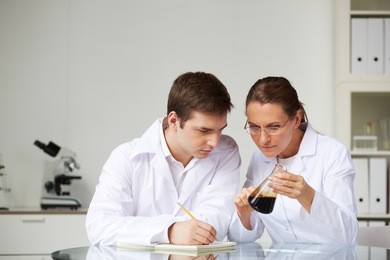 two scientists looking at glass flask with liquid oil in laboratory while analyzing its characteristics