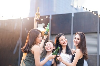 group of young cute asian girl gang best friends having party at rooftop restaurant. girls drinking beer alcohol and toasting bottle feeling happy enjoy, fun with smile face. night lifestyle concept.