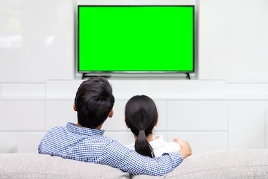 back view of asian couple sitting on sofa relaxing and enjoy watching tv at home with green screen