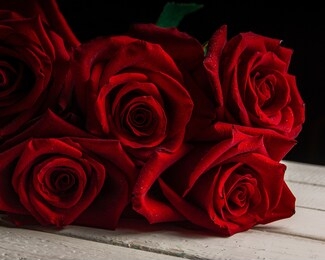 a bouquet of red roses covered with small drops of water lying on a white wooden table