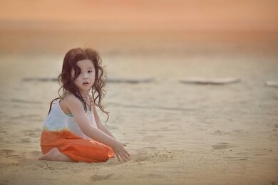 adorable asian child with curly hair playing sand at the beach.orange sunset.little girl wearing colorful dress for outdoor.beachwear for kid.young female having fun on vacation.