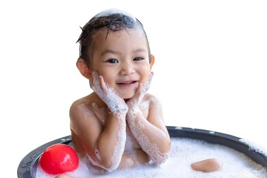 portrait image of 1-2​ years old baby. happy baby asian girl take a bath with bubbles soap. she sitting in a bathtub and playing with a ball toy. sweet smiling. on white background isolated.