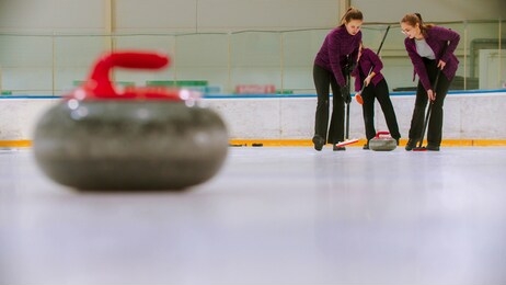 curling training - leading granite stone on the ice - two women rubbing the ice before the stone