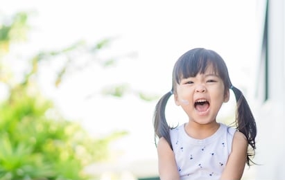 adorable toddler girl putting solar cream on arms hands smiling happy outdoors by pool under sunshine on beautiful summer day.mixed race asian / caucasian kid girl.sunscreen or sunblock and skincare.