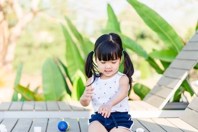 adorable toddler girl putting solar cream on arms hands smiling happy outdoors by pool under sunshine on beautiful summer day.mixed race asian / caucasian kid girl.sunscreen or sunblock and skincare.