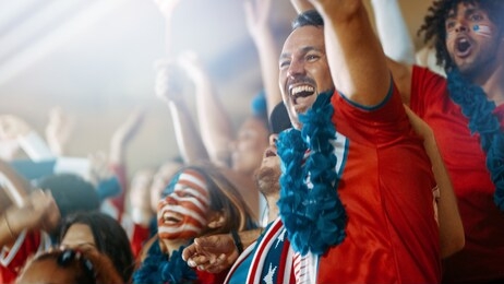excited usa football fans and supporters celebrating a goal being scored in the sports stadium. american soccer fans cheering their team in the stands.