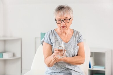 senior woman suffering from parkinson syndrome with glass of water in clinic