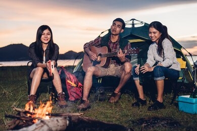 camping tent camp in nature happy young asian friends group people in night party bonfire and the man playing guitar together girlfriend in summer at nature forest, outdoor holidays summertime concept