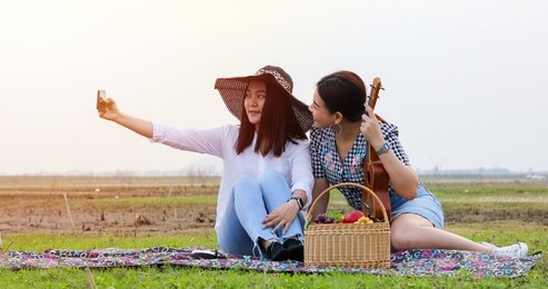 a group of asian friends playing ukelele and spending time making a picnic in the summer holidays.they are happy and selfie ,relax time on holiday concept travel