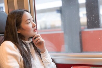 an asian woman is sitting happily looking at the natural view from the window on the train and traveling on a vacation in switzerland and planning a train trip.