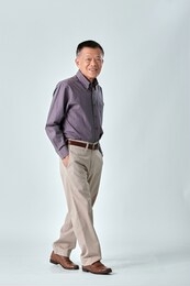 full body of an asian old man wear purple shirt and beige pants walking and keep his hands in his pockets in studio white  background. isolated picture of happiness asian old man.