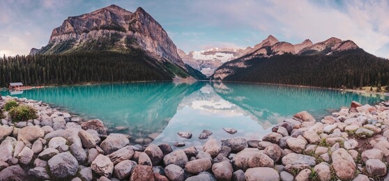 a panoramic photo of lake louise, mountain peaks, turquoise lake reflections, jumbo stones, a row of orange canoes sitting on a jetty by the boat house at sunrise in banff national park, ab, canada.