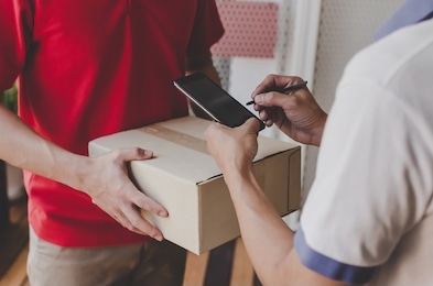 man customer using pen signature on digital mobile phone with delivery man in red uniform for receiving parcel post box from courier at home, express home delivery service and shopping online concept
