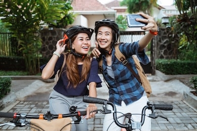 two asian young woman wearing helmet and bags with camera cellphone make a video content on folding bike before go to campus