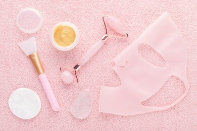 golden facial cream mask with a brush, jade roller and silicone beauty mask on pink background