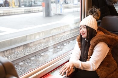 an asian woman is sitting happily looking at the natural view from the window on the train and traveling on a vacation in switzerland and planning a train trip.