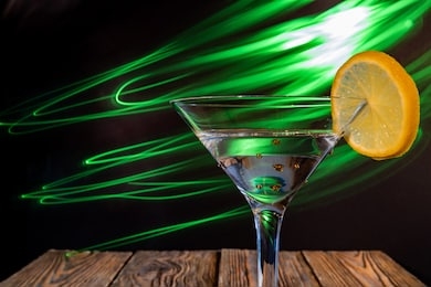 a glass of martini with a cocktail, with the effect of neon lights, on a black background and an old wooden table, close-up, blurred background, shallow depth of field. concept, club party.