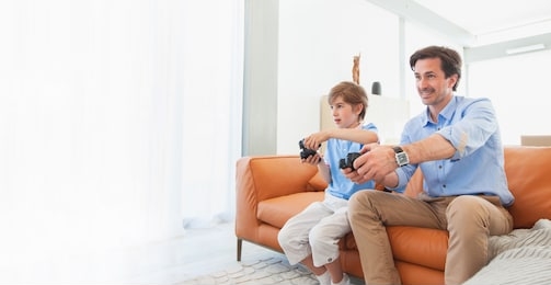 father and son with video game controllers smiling playing game at home