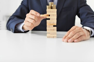 male bank manager near tower made of blocks with coins sitting at table in office. concept of planning, risk and strategy in business