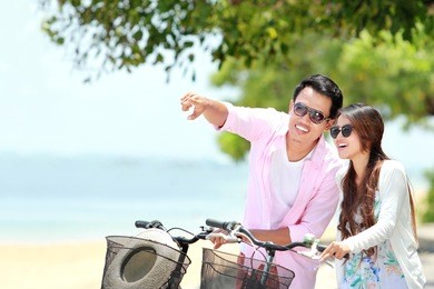happy asian young couple with bicycle on the beach having fun together