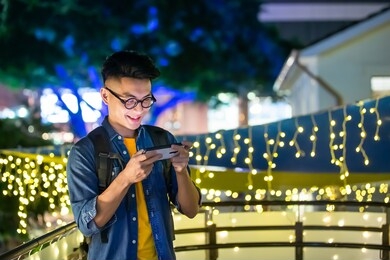 asian young man paly mobile games on smart phone outdoor in the evening
