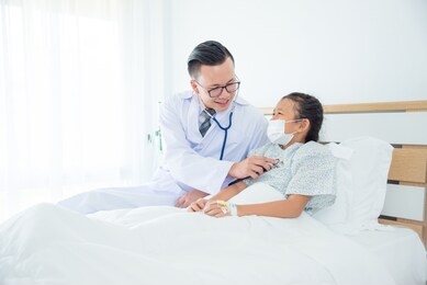 young asian male doctor visiting his child patient at bed in hospital ward. doctor listening patient lung sound by stethoscope .
