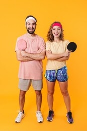 portrait of athletic young couple wearing headbands holding rackets while playing table tennis together isolated over yellow background