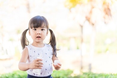 adorable toddler girl putting solar cream on arms hands smiling happy outdoors by pool under sunshine on beautiful summer day.mixed race asian / caucasian kid girl.sunscreen or sunblock and skincare.