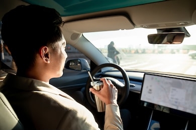 asian relaxed man use reusable eco-friendly ecological straw to drink while riding an autonomous self driving electric car and turn on autopilot function