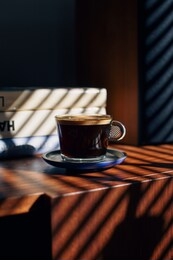 coffee cup on a brown table with books and speaker behind. 