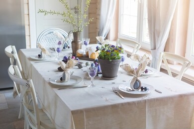 easter festive spring table setting decoration, bunny ears shaped napkins, dyed hen's and quail eggs, cakes, violets potted, feathers, family dinner or breakfast concept, banner