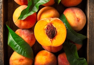 peaches with leaves in a wooden box with peach in halves on top. flat lay composition with ripe juicy peaches. harvest of peaches for food or juice. top view fresh organic fruit, vegan food.